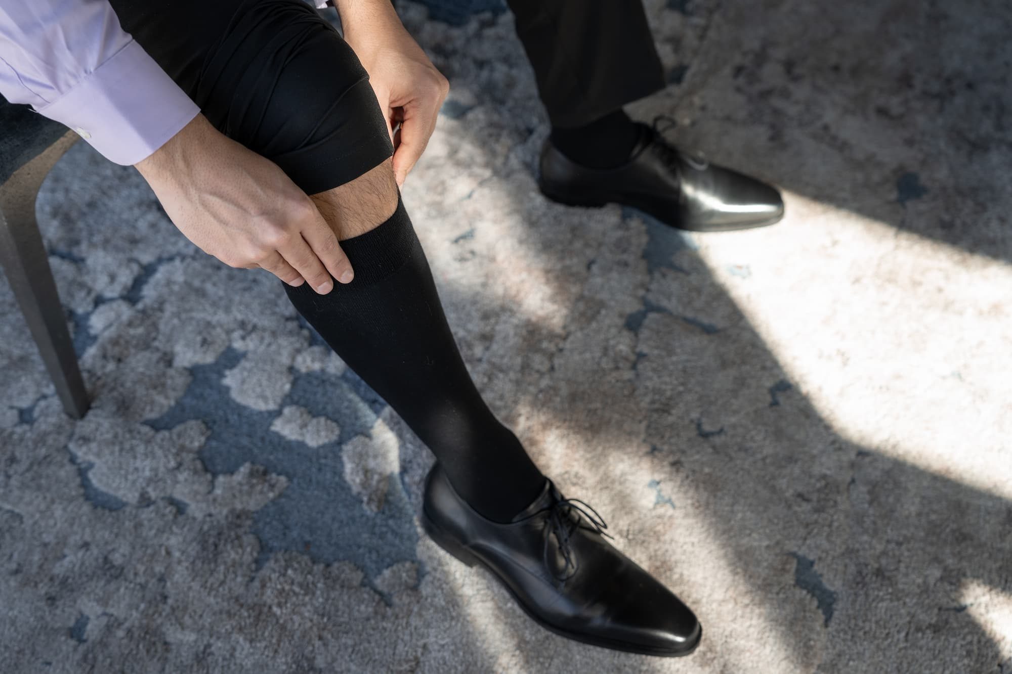 Businessman wearing compression socks. Closeup top view. no face. Pulling up the sock. wearing official office outfit, classic shoes.
