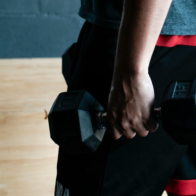 Close-up of a man holding dumbbells down by his sides on a wooden floor