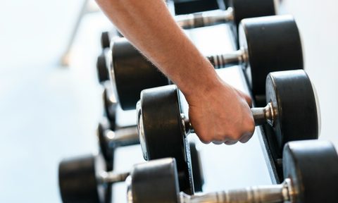 Close-up man hand grabbing dumbbell from rack weight rack in gym