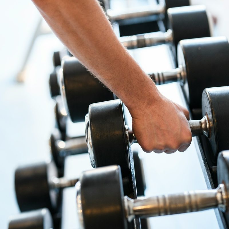 close up man hand grabbing dumbbell from rack weight rack in gym