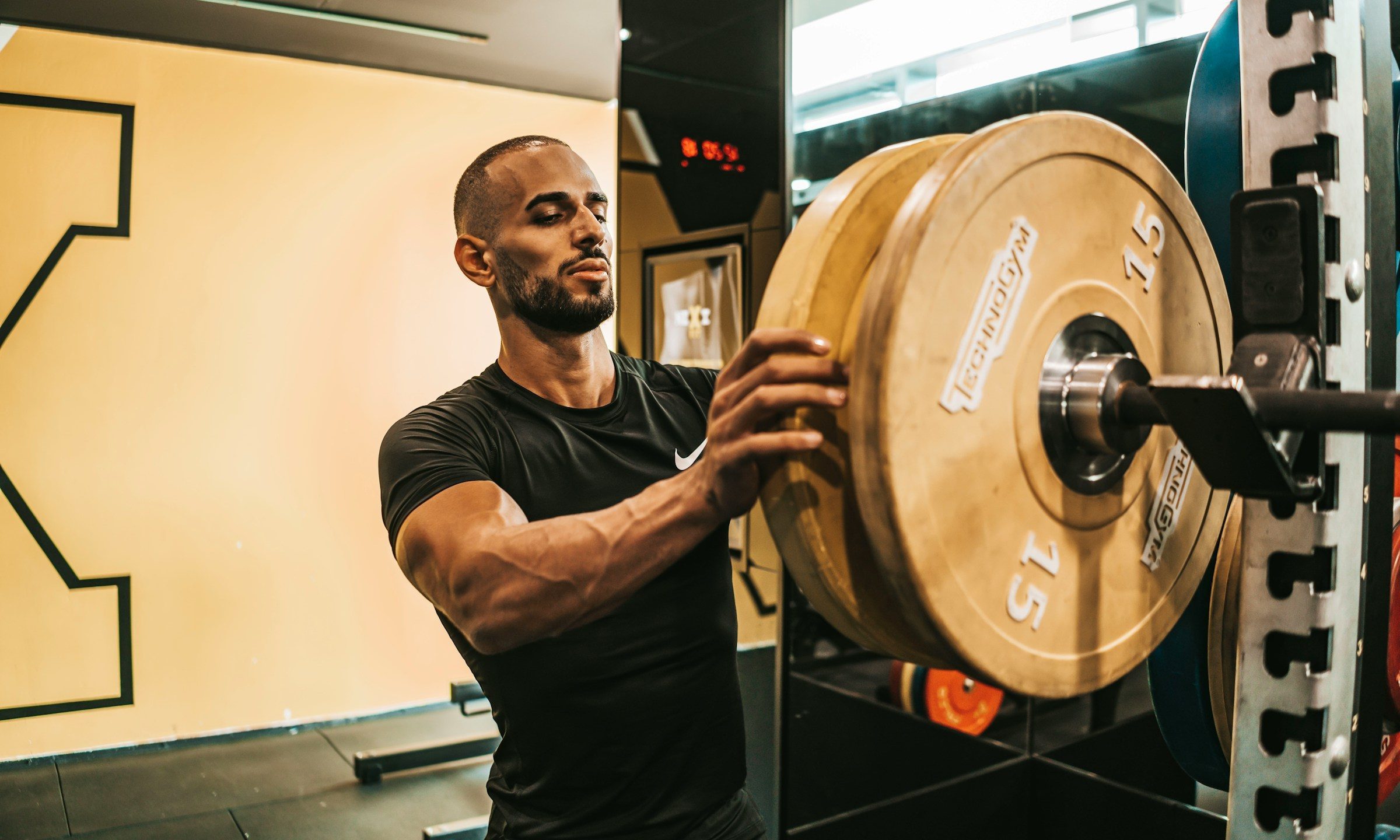man putting weights on barbell on rack in gym black t shirt
