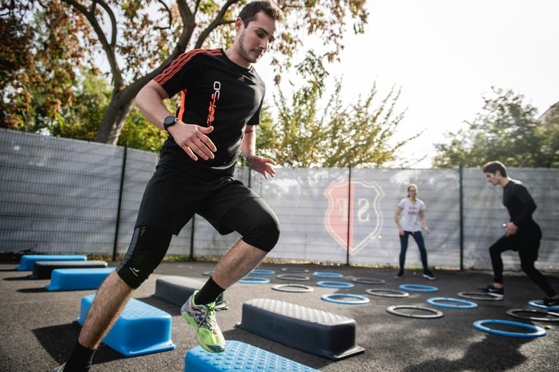 man wearing black t shirt exercising outdoors outside with blue steps