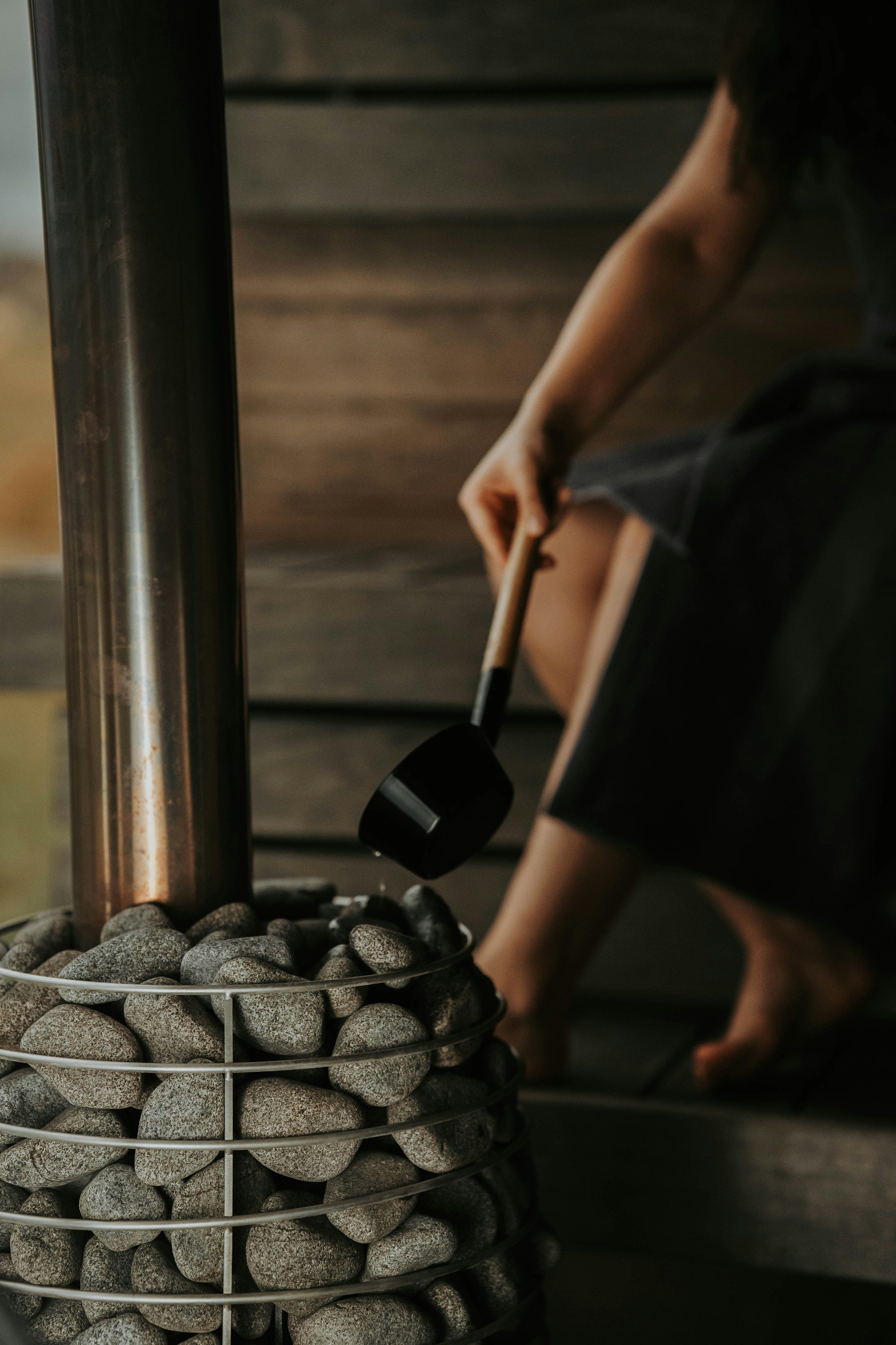 close up of woman's arm pouring water on hot stones to produce steam in a sauna room