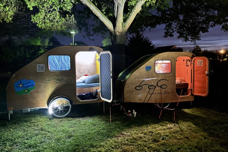 Two i:woody wooden teardrop trailers at a campsite at night.