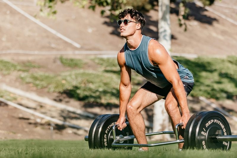 Man outside wearing blue sleeveless shirt doing trap bar deadlift in nature