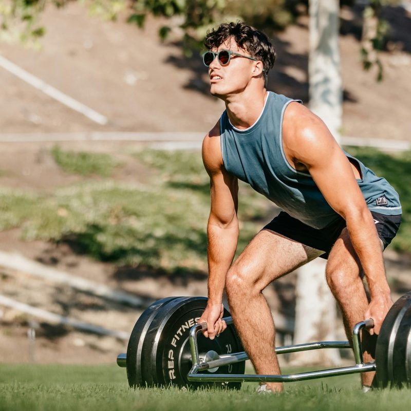 Man outside wearing blue sleeveless shirt doing trap bar deadlift in nature