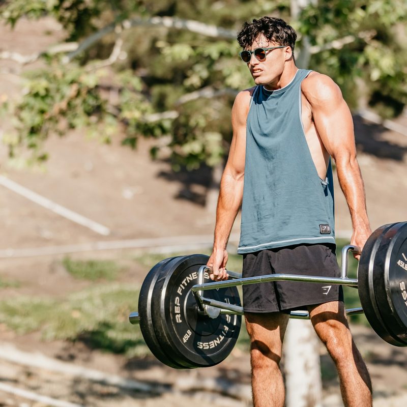 Man outside wearing sleeveless shirt in nature doing trap bar deadlift hex bar
