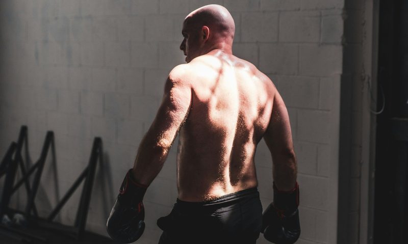shirtless man wearing black shorts walking wearing boxing gloves