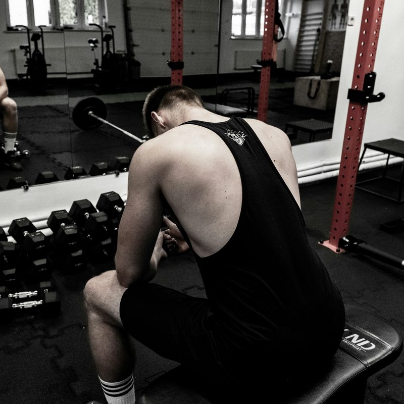Man sitting in gym head down next to dumbbells weight rack