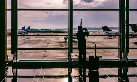 man standing in an airport with his suitcase next to him