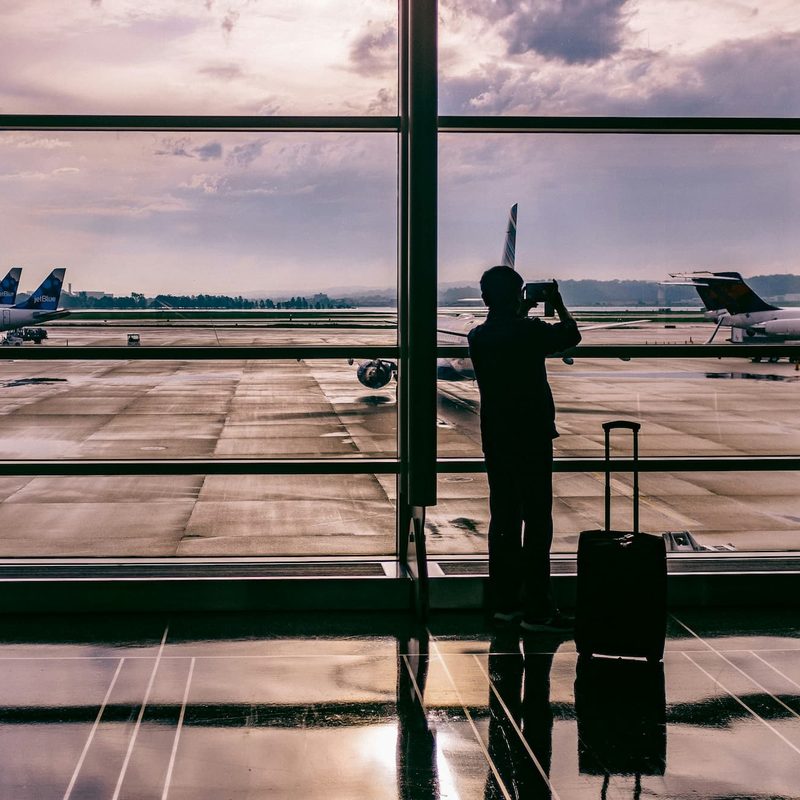 man standing in an airport with his suitcase next to him