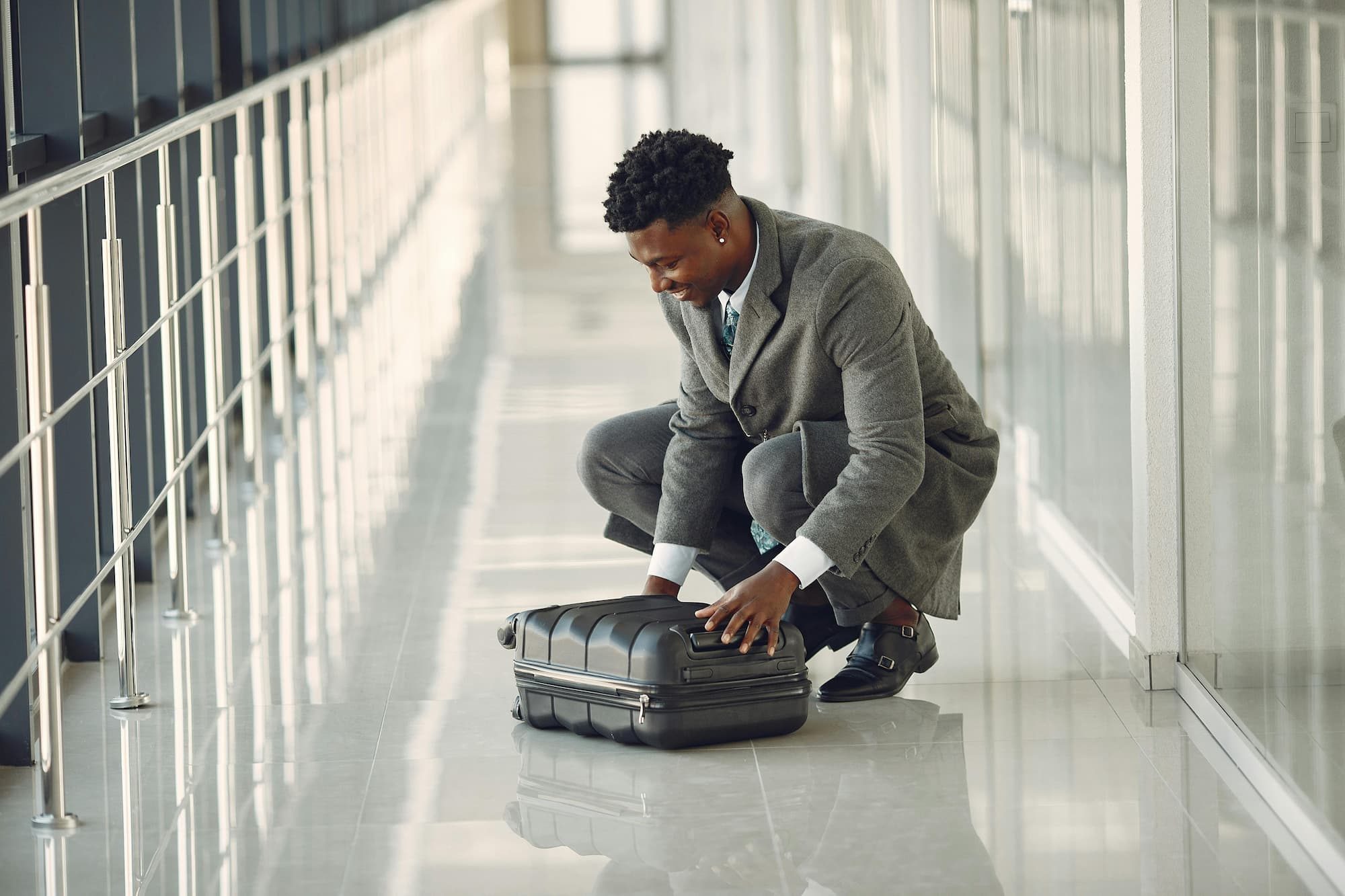 man in suit sitting on the ground in airport looking at suitcase