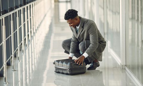 Man in suit sitting on the ground in airport looking at suitcase