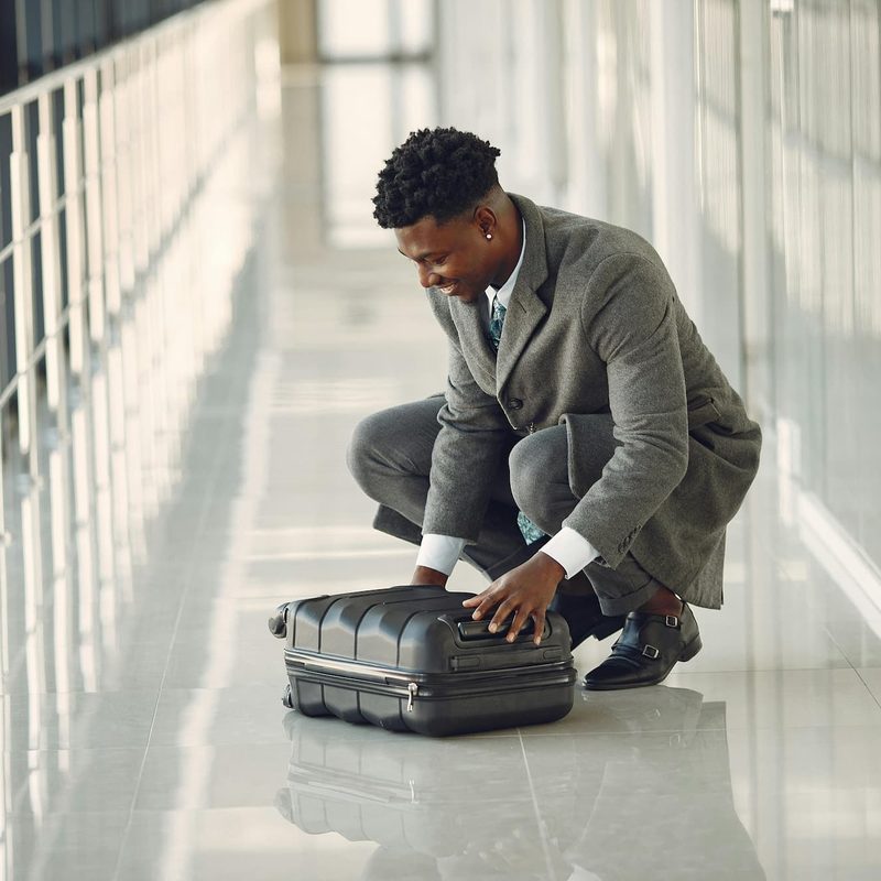 Man in suit sitting on the ground in airport looking at suitcase