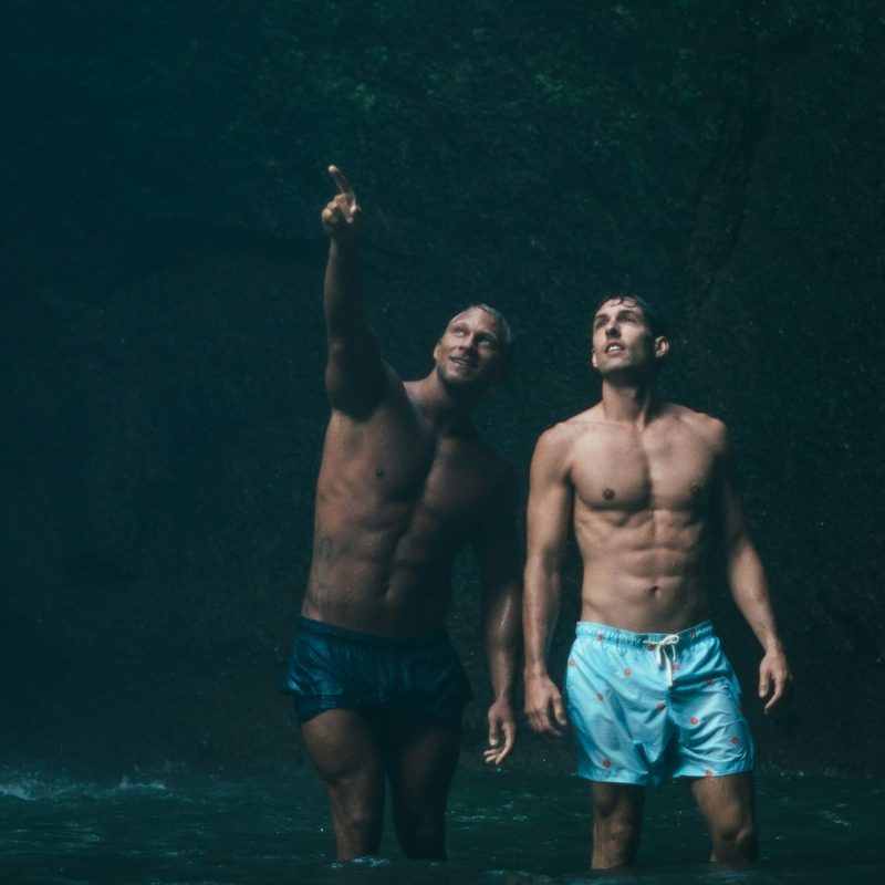 Two men standing outside in nature by a waterfall one pointing