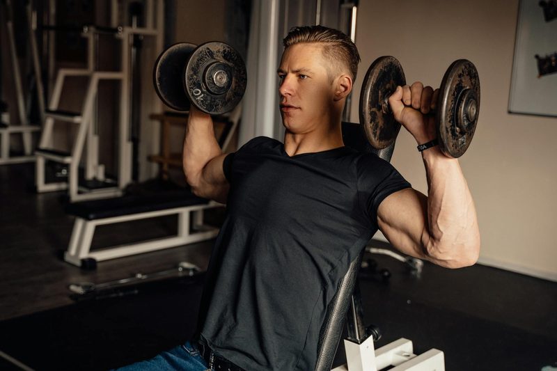 Man with black t shirt doing arnold press dumbbell press exercise in gym