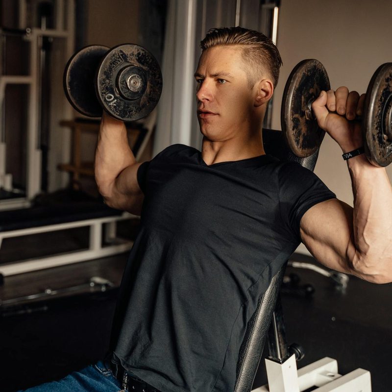 Man with black t shirt doing arnold press dumbbell press exercise in gym