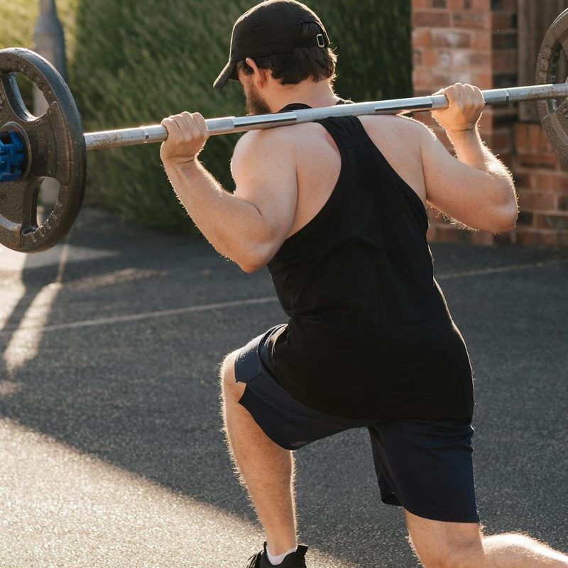 Man doing barbell lunge outside brick wall