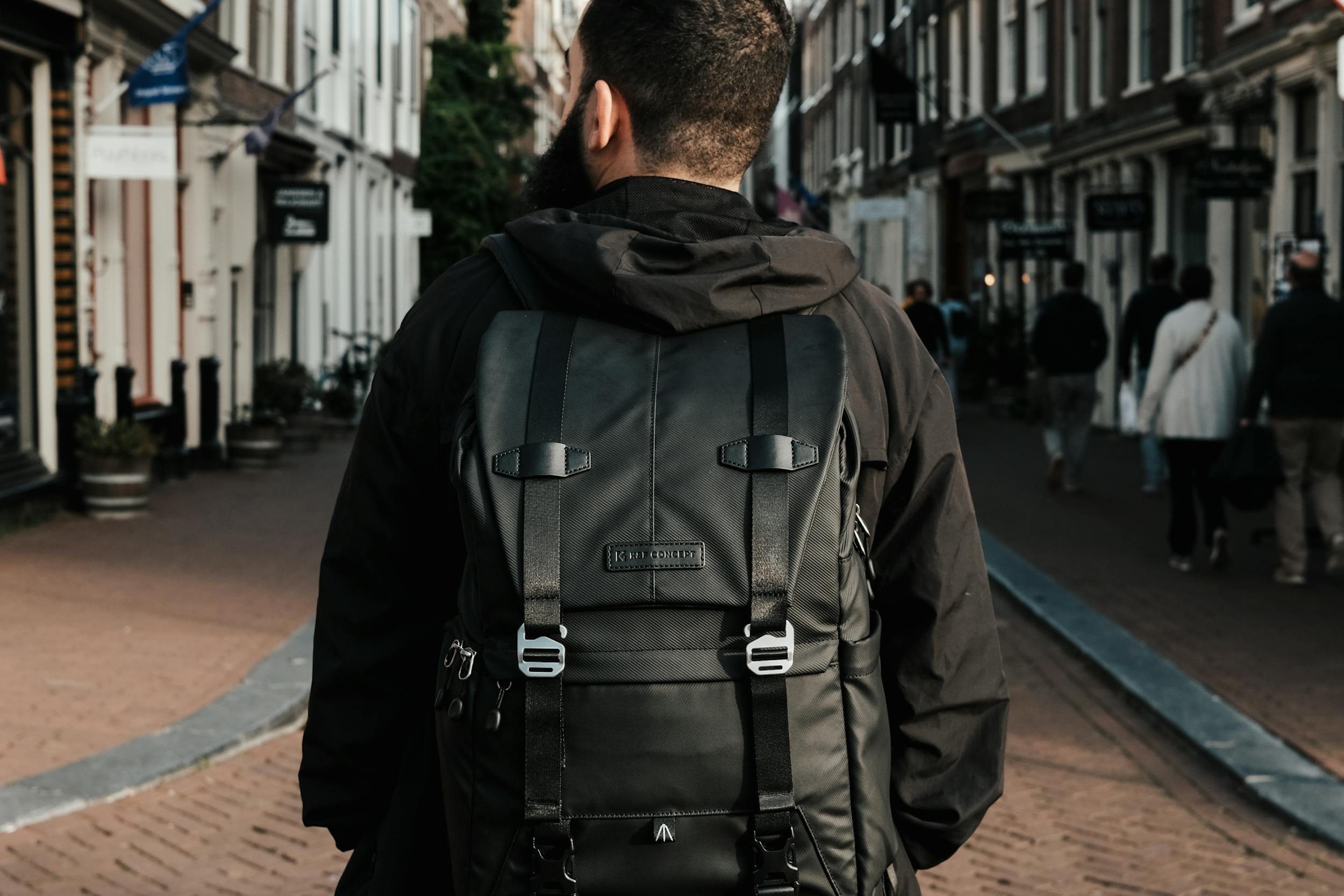 man wearing black backpack walking rucking outside through city streets