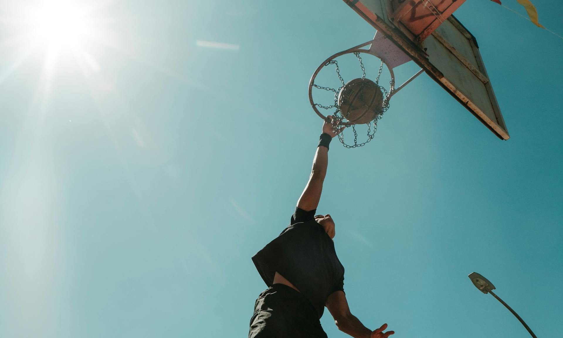 jumping man playing basketball putting in hoop outside blue sky