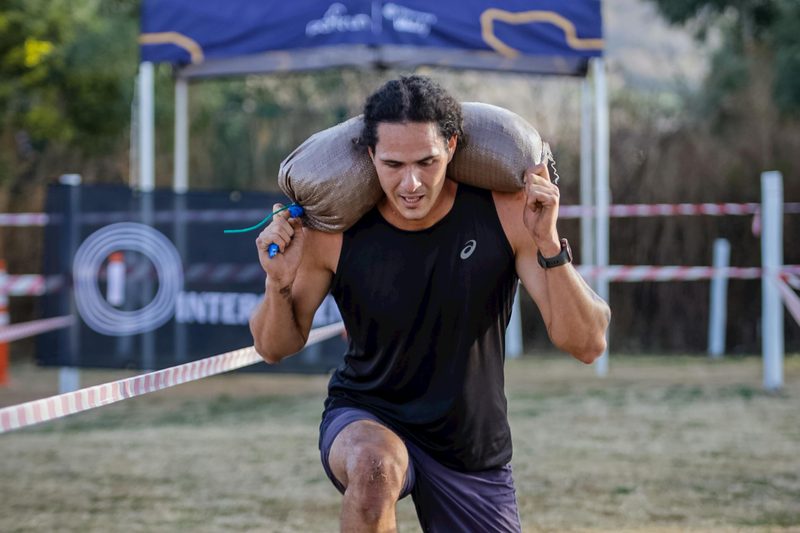 man doing walking lunge outside carrying weight on back on grass