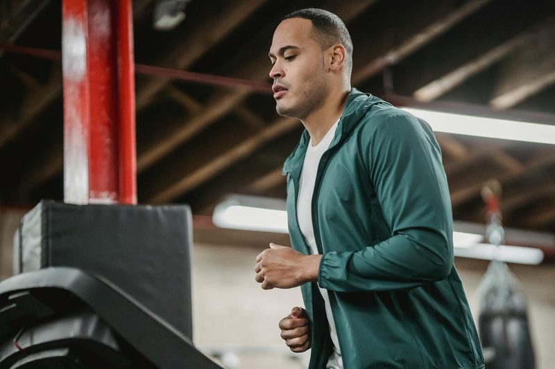 Man running on treadmill wearing blue jacket in gym