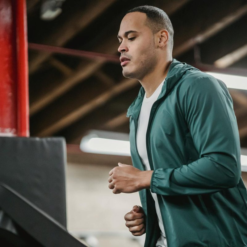 Man running on treadmill wearing blue jacket in gym