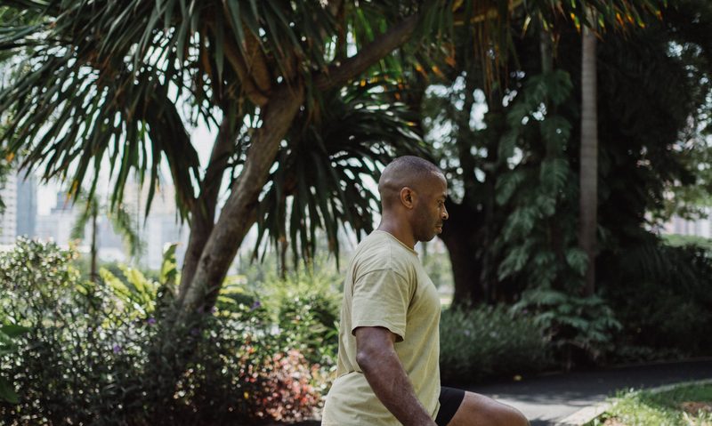 man doing walking lunge outside by palm tree