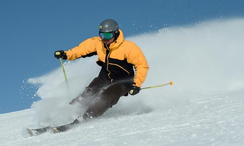 Man skiing on slopes wearing yellow jacket Nordic poles sunglasses