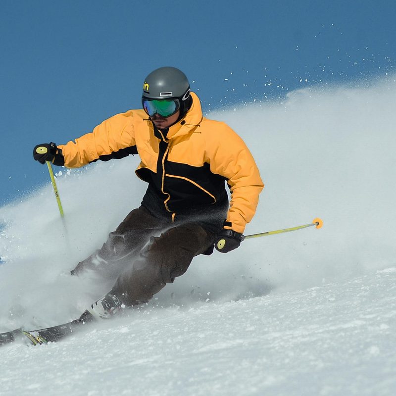 Man skiing on slopes wearing yellow jacket Nordic poles sunglasses