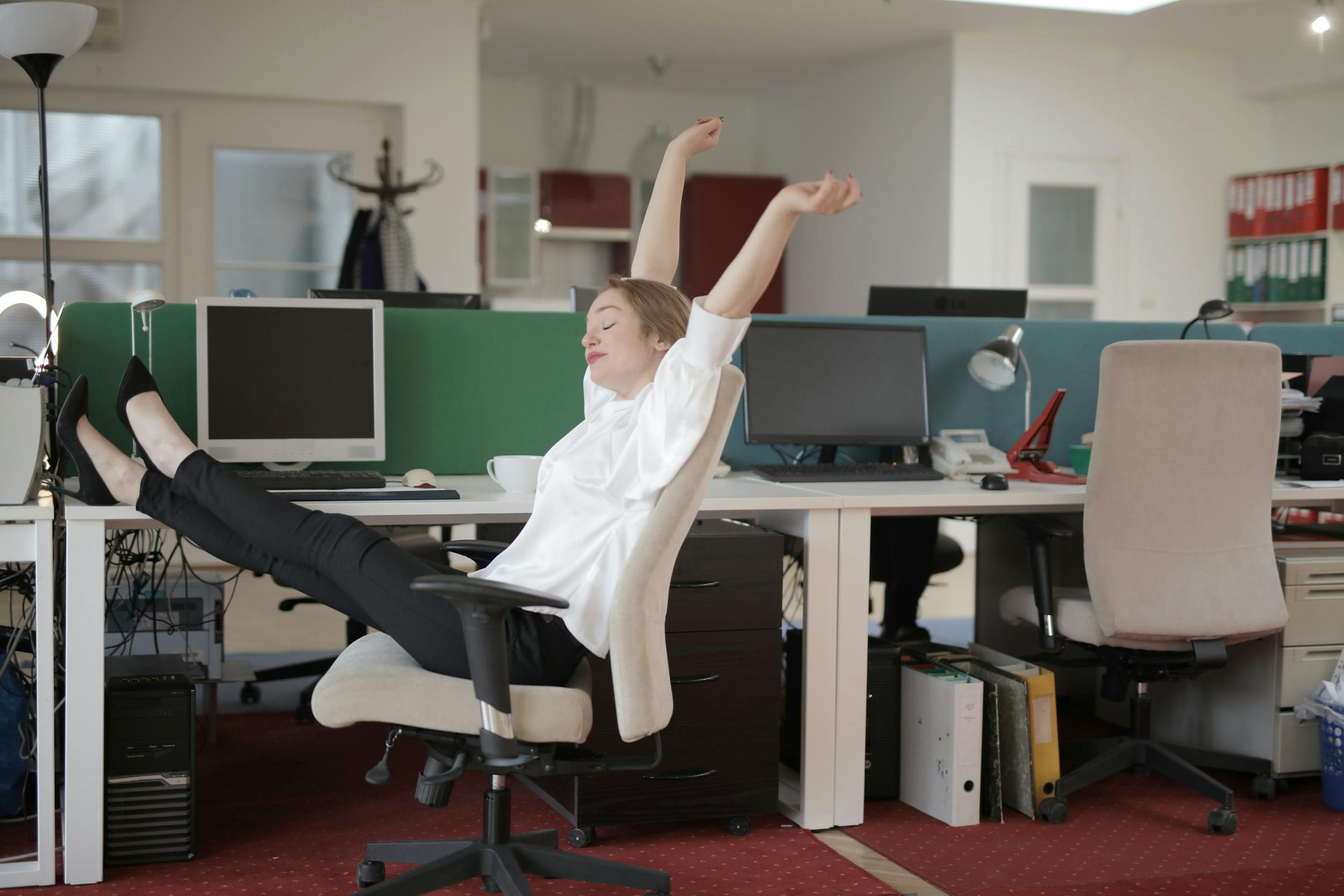 woman white shirt in office by computer stretching legs at desk
