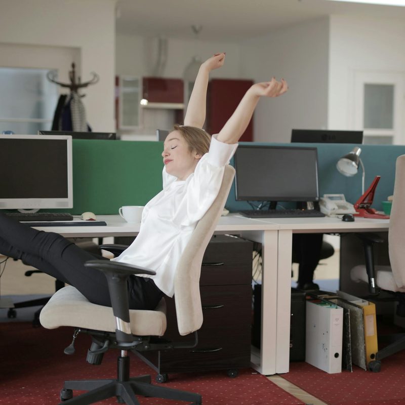 Woman in an office by a computer stretching legs at her desk