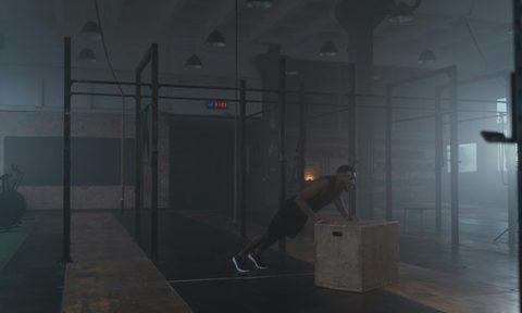 man doing incline push up in gym on wooden plyo box dark room