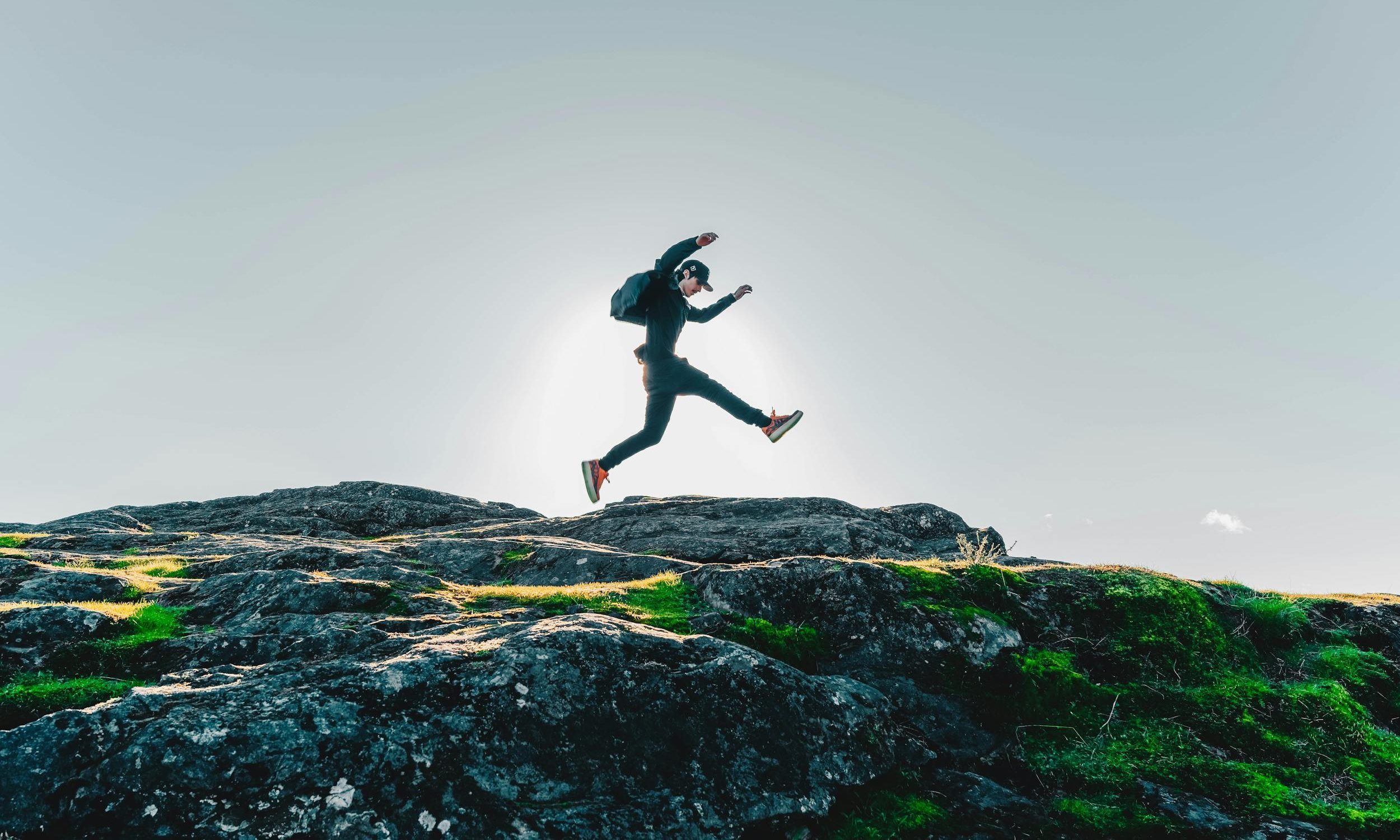 man rucking jumping walking backpack rucksack on rocks blue sky hat happy man