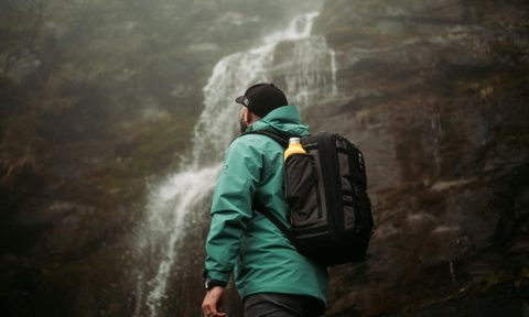 Man wearing green and hat rucking backpack rucksack walking in nature by waterfall with drink water