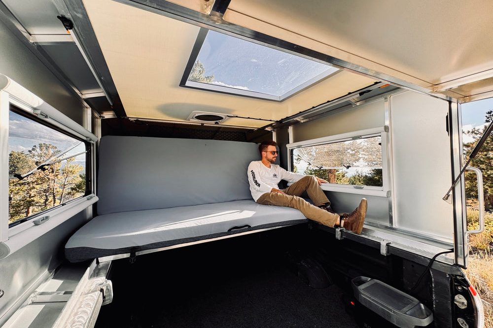 Man sitting on the convertible bed/couch inside the Moonlander X hardshell truck camper.