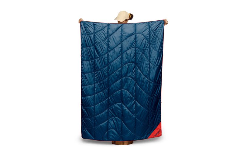 Woman holding up a Rumpl Backcountry Puffy camping blanket against a plain white background.