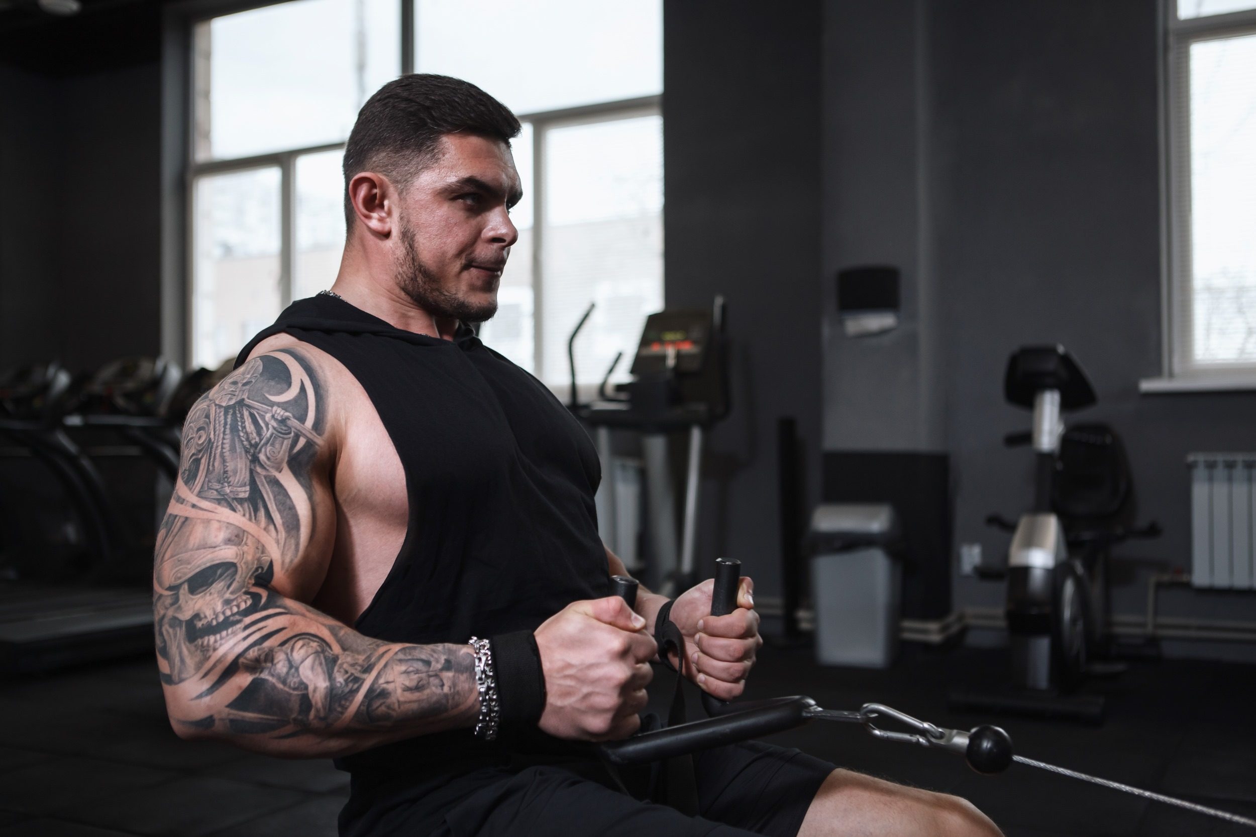Man with tattoos sitting in the gym doing seated cable rows exercise with cable machine
