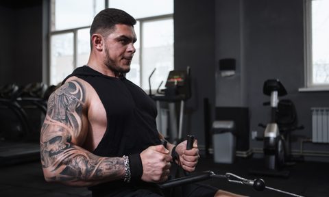 Man with tattoos sitting in the gym doing seated cable rows exercise with cable machine
