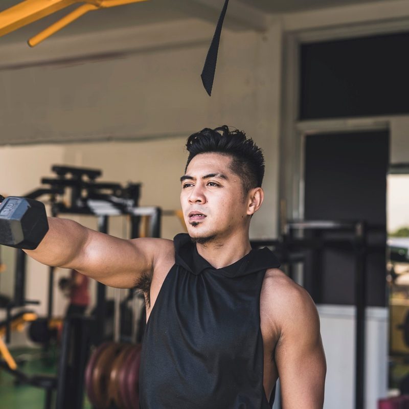 man doing one arm dumbbell front raise exercise in gym