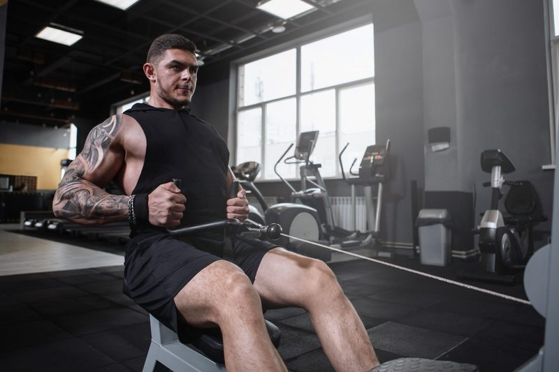 Man sitting in gym doing seated cable row on cable machine