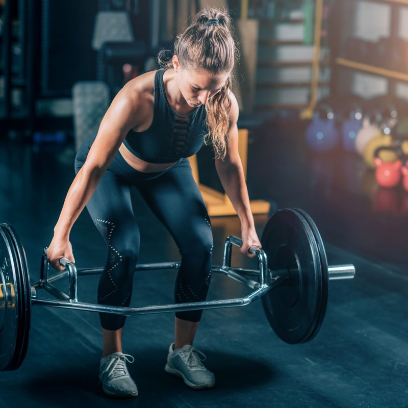 Woman in the gym with leggings doing a trap bar deadlift exercise hex bar