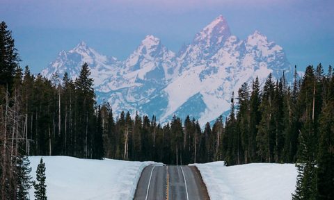 A paved road in the middle of the snow with snow covered mountains ahead