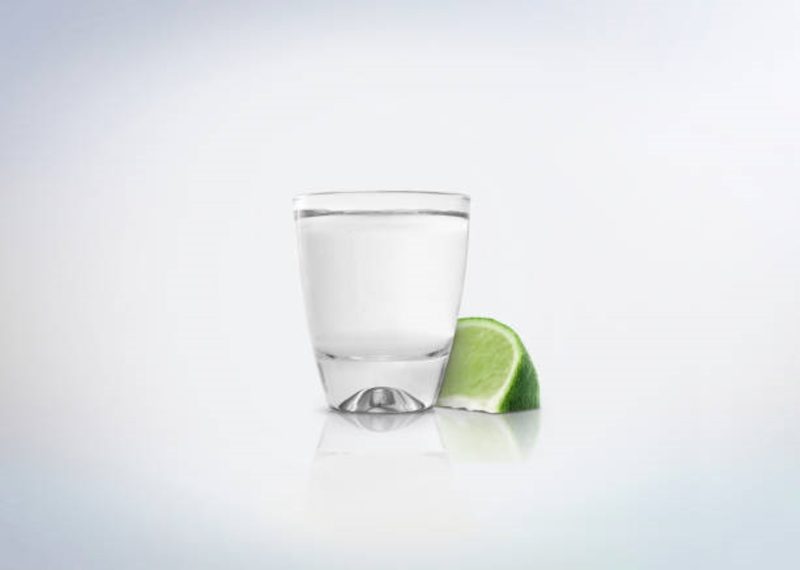 Tequila in shot glass next to a slice of lime