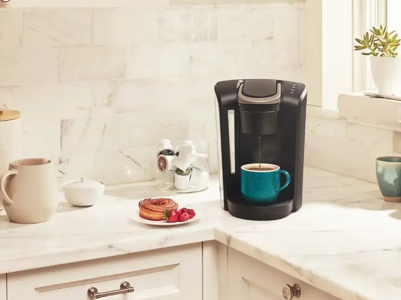 A Keurig - K-Select Single-Serve K-Cup Pod Coffee Maker sitting in a kitchen corner with a cup of freshly brewed coffee nearby.