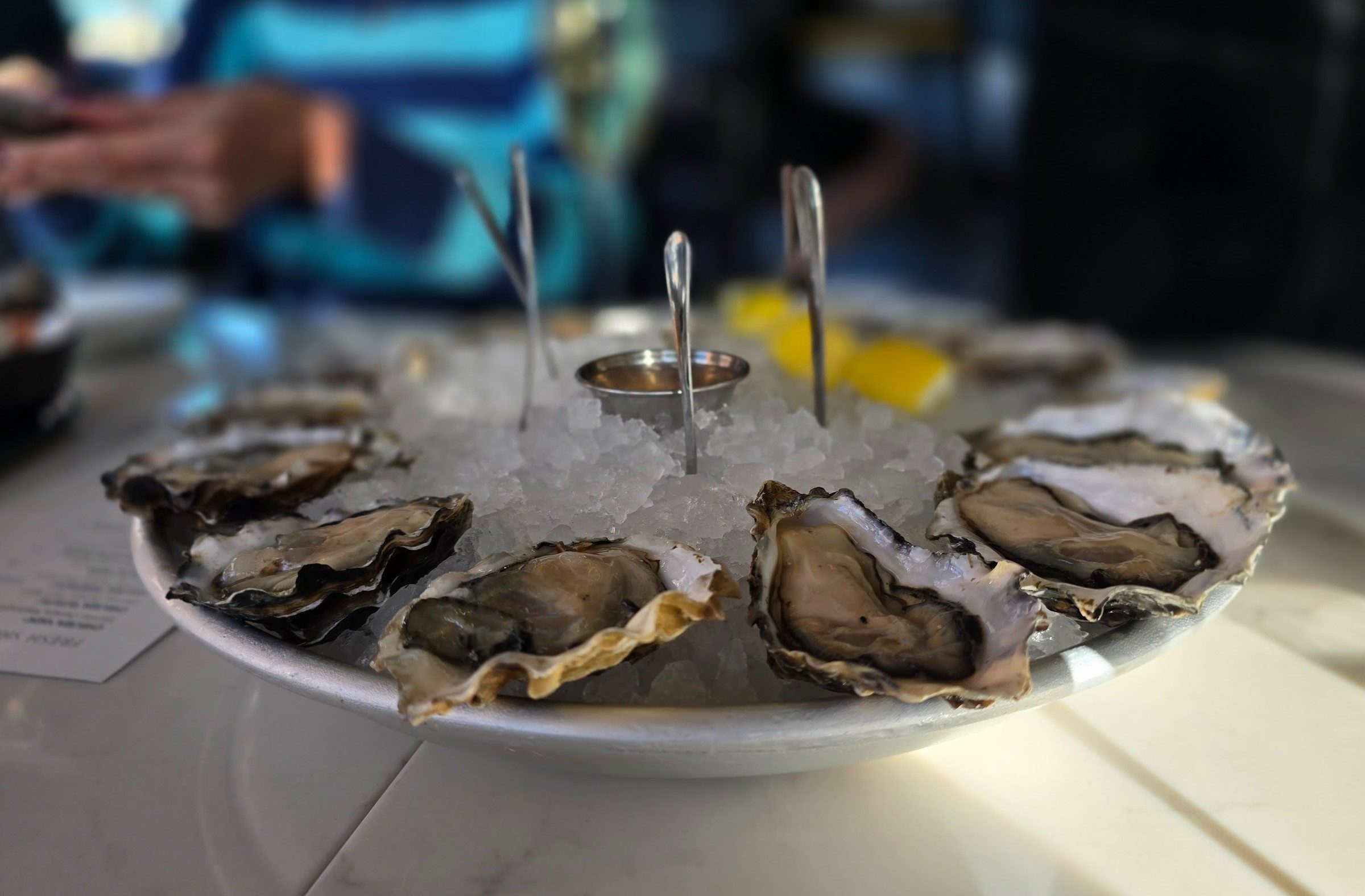 a dozen of oysters over ice with three forks and lemon slices