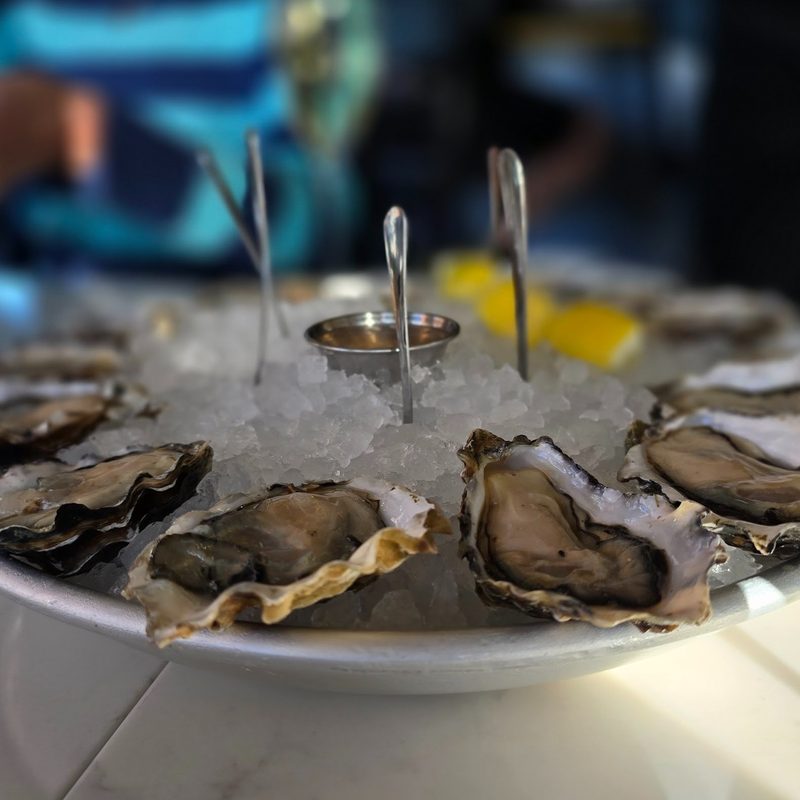 a dozen of oysters over ice with three forks and lemon slices