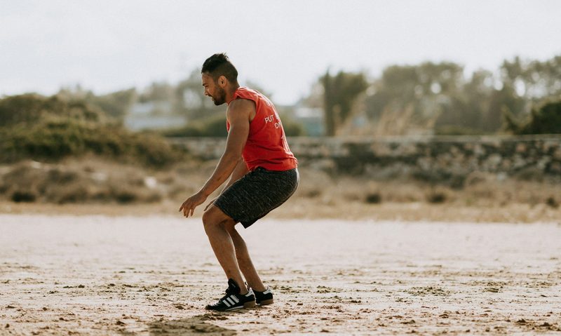 Man wearing red shirt jump squat jumping in sand