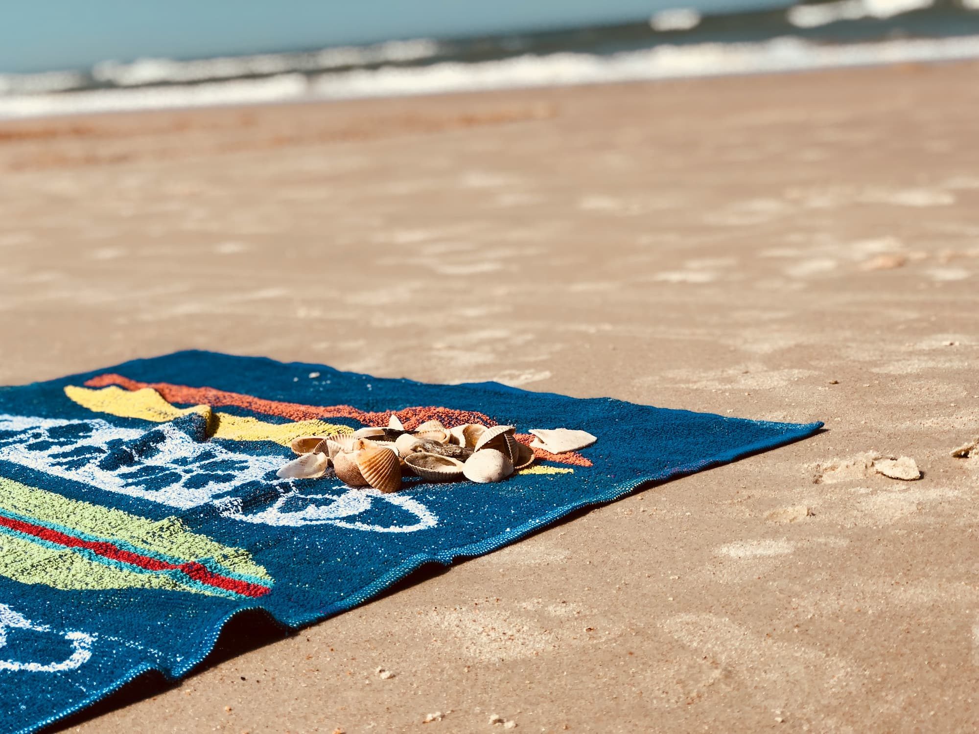 beach towel with seashells on top on the sand