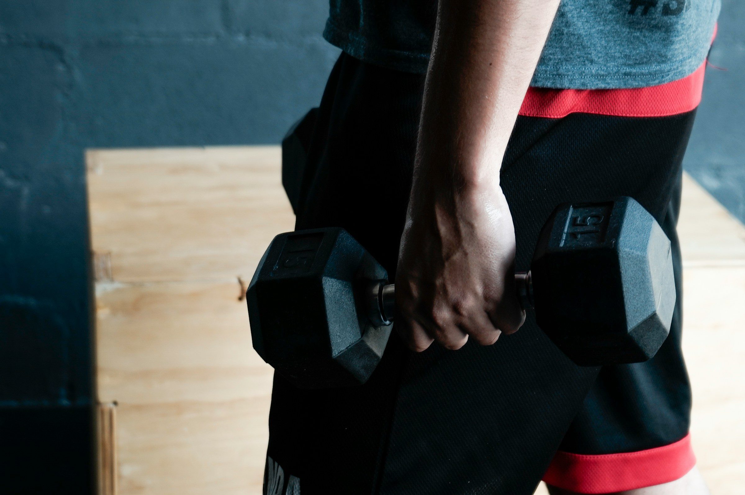man holding dumbbell red black shorts wooden floor dumbbell shrug